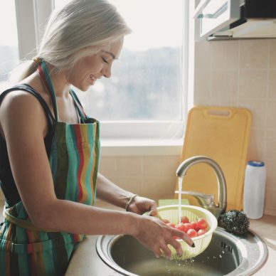 Young woman washing fresh vegetables tomatoes in kitchen under water stream, preparation salad vegetarian meal