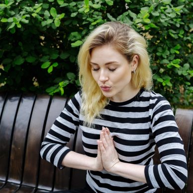 girl doing yoga exercise and meditation sitting on a bench in a park in striped top