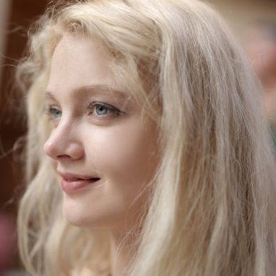 A portrait of a young blonde female with a beautiful smile with a blurred background