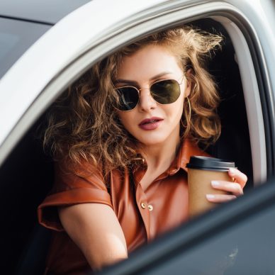 Fashion portrait of young woman in in white car with cup or coffee or tea.