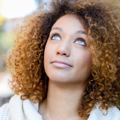 Beautiful young African American woman with afro hairstyle and green eyes wearing white winter dress with autumn leaves in the background.