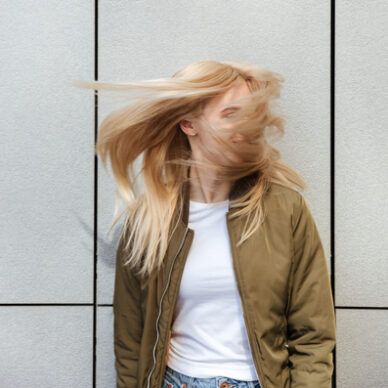 Funny blonde woman shaking her hair against grey wall