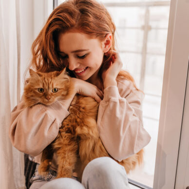 Relaxed smiling girl playing with her fluffy cat. Indoor shot of amazing lady holding pet.