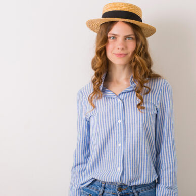 portrait of young pretty woman in straw hat jeans blue cotton shirt posing on white wall, natural look, innocent face, summer fashion trend accessories, curly blond hair
