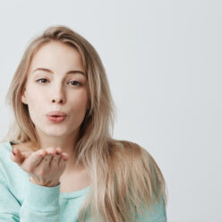 Attractive caucasian woman posing with kiss on her lips with blonde dyed hair, having flirty look feeling confident and beautiful. Charming female model sending kisses to camera, saying goodbye