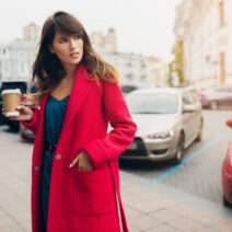 stylish woman in red coat walking in street with coffee